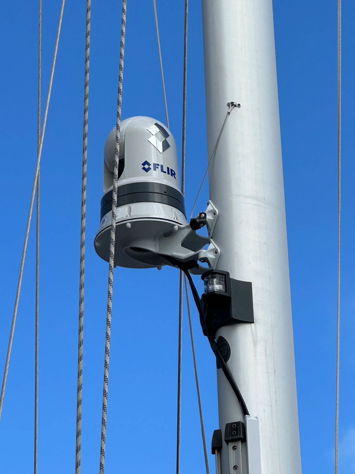 Scanstrut CAM-MM-03 camera mast mount holding a FLIR camera on a sailboat mast against blue sky